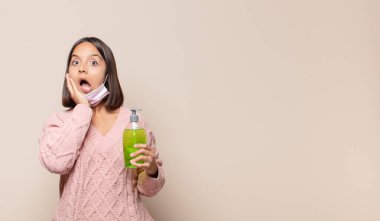 Genç kadın şok olmuş ve korkmuş hissediyor, ağzı açık ve elleri yanaklarında korkmuş görünüyor.