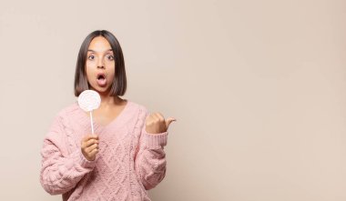 İnançsızlıktan hayrete düşmüş genç bir kadın, yan taraftaki objeyi işaret ederek, 