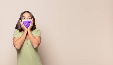 Genç kadın şok olmuş ve korkmuş hissediyor, ağzı açık ve elleri yanaklarında korkmuş görünüyor.