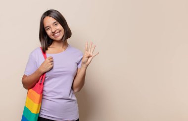 Genç bir kadın gülümsüyor ve arkadaş canlısı görünüyor, 4 ya da 4 numarayı gösteriyor, eli önde, geriye doğru sayıyor.