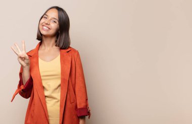 Genç bir kadın gülümsüyor ve arkadaş canlısı görünüyor. Üç ya da üç numarayı gösteriyor. Elleri önde, geri sayıyor.