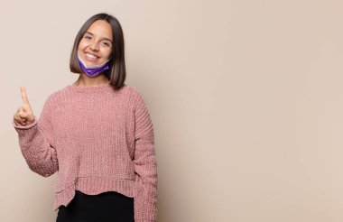 Genç bir kadın gülümsüyor ve arkadaş canlısı görünüyor, bir numarayı gösteriyor ya da ilk eli önde, geri sayıyor.