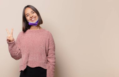 Genç bir kadın gülümsüyor ve arkadaş canlısı görünüyor. İki ya da iki numarayı gösteriyor. Elleri önde, geri sayıyor.