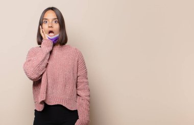 Genç kadın şok olmuş ve korkmuş hissediyor, ağzı açık ve elleri yanaklarında korkmuş görünüyor.