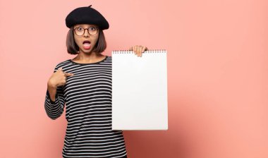 Genç kadın sanatçı mutlu, şaşırmış ve gururlu hissediyor. Heyecanlı ve şaşkın bir bakışla kendini işaret ediyor.