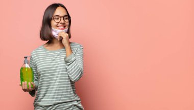 Gülümseyen mutlu, kendine güvenen bir yüz ifadesi olan genç bir kadın. Elleri çenesinde, merak ediyor ve yan tarafa bakıyor.
