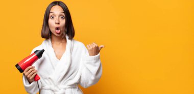 İnançsızlıktan şaşkın şaşkın bakıyor, yan taraftaki objeyi işaret ediyor ve 