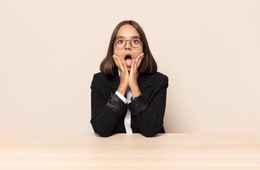 Şok olmuş ve korkmuş hissediyorum, ağzı açık ve elleri yanaklarında korkmuş görünüyor.