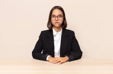 Şaşırmış ve kafası karışmış görünüyor, sinirsel bir hareketle dudağını ısırıyor, sorunun cevabını bilmiyor.