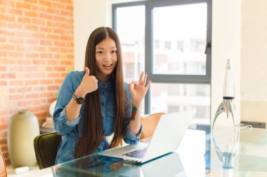 Genç Asyalı kadın kendini mutlu, şaşkın, tatmin olmuş ve şaşırmış hissediyor, tamam gösteriyor ve el kol hareketleri yapıyor, gülümsüyor.
