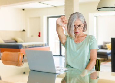 Orta yaşlı bir kadın sinirli, sinirli, hayal kırıklığına uğramış ya da canı sıkkın, ciddi bir bakışla başparmağını kaldırıyor.
