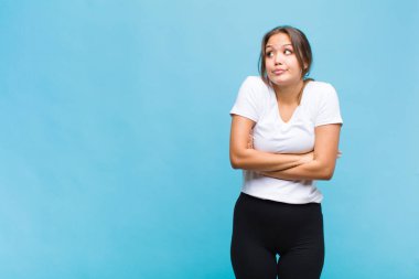 Genç İspanyol kadın omuz silkiyor, kafası karışık ve emin değil, kolları bağlı ve şaşkın görünüyor.