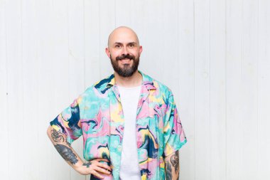 Kel adam mutlu bir şekilde gülümsüyor, eli kalçasında ve kendinden emin, olumlu, gururlu ve arkadaş canlısı.