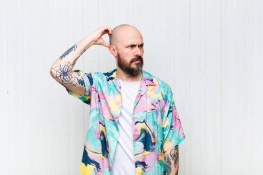 Kel adam şaşkın ve kafası karışmış hissediyor, kafasını kaşıyor ve yan tarafa bakıyor.