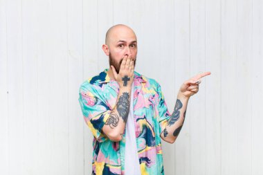 Kel adam kendini mutlu, şaşkın ve şaşırmış hissediyor. Ağzını eliyle kapatıyor ve yanal kopya alanını işaret ediyor.