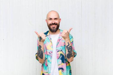 Kel adam neşeyle gülümsüyor ve mutlu görünüyor, kaygısız ve pozitif hissediyor.