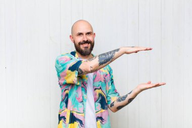 Kel adam gülümsüyor, mutlu, pozitif ve tatmin olmuş hissediyor, fotokopi alanında nesne veya konsept tutuyor veya gösteriyor