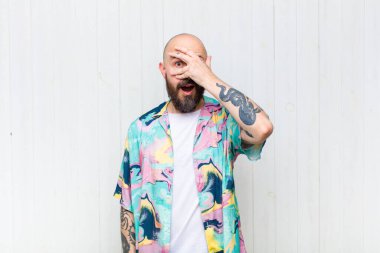 Kel adam şok olmuş, korkmuş ya da korkmuş görünüyor. Yüzü elle örtülmüş ve parmaklarının arasından gizlice bakıyor.