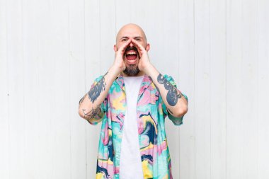 Kel adam mutlu, heyecanlı ve pozitif hissediyor. Elleri ağızda, bağırarak bağırıyor.