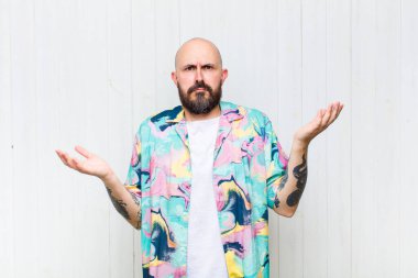 Kafası karışmış, kafası karışmış ve stresli görünen kel bir adam, farklı seçenekler arasında merak ediyor, kararsız hissediyor.