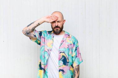 Kel adam stresli, yorgun ve hayal kırıklığına uğramış görünüyor, alnından ter damlıyor, umutsuz ve bitkin hissediyor.