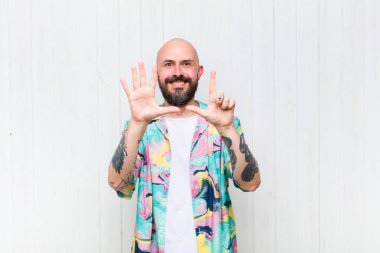 Kel adam gülümsüyor ve dost canlısı görünüyor, 7 ya da 7 numarayı gösteriyor, eli önde, geri sayıyor.