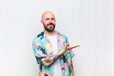 Kel adam mutlu bir şekilde gülümsüyor, mutlu hissediyor ve fotokopi alanında avucuyla bir konsept gösteriyor.