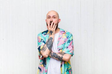 Kel adam şok ve inançsızlık içinde, elleri yanak ve kolları çaprazlanmış, sersemlemiş ve şaşırmış hissediyor.