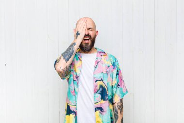 Kel adam uykulu görünüyor, sıkılmış ve esniyor, baş ağrısı ve yüzünün yarısını kaplayan bir eliyle