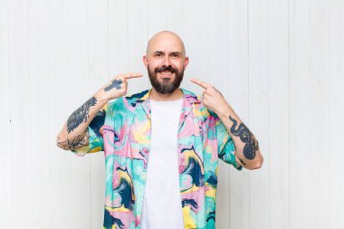 Kel adam kendine güvenerek gülümsüyor. Geniş gülüşünü gösteriyor. Olumlu, rahat, tatmin olmuş bir tavır.