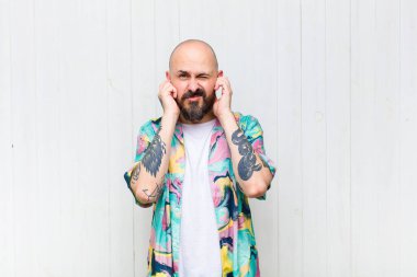 Kel adam sinirli, stresli ve sinirli görünüyor, iki kulağını da sağır edici bir ses, ses ya da yüksek sesle kapatıyor.