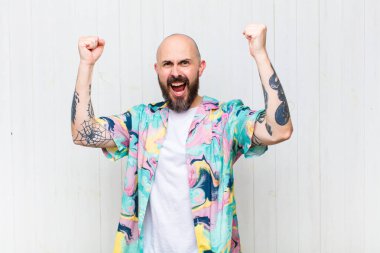 Kel adam muzaffer bir şekilde bağırıyor, heyecanlı, mutlu ve şaşırmış görünüyor.