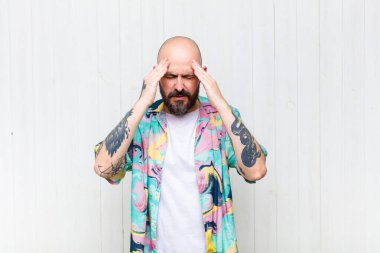 Kel adam stresli ve hayal kırıklığına uğramış görünüyor, baskı altında çalışıyor ve başı ağrıyor.