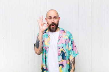 Kel adam kendini başarılı ve tatmin olmuş hissediyor, ağzı açık gülümsüyor, elle işaret veriyor.