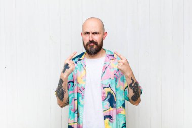 Kel ve kötü tavırlı bir adam gururlu ve agresif görünüyor, yukarıyı işaret ediyor ya da elleriyle alay işareti yapıyor.