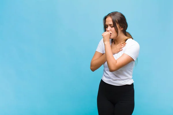 young hispanic woman feeling ill with a sore throat and flu symptoms, coughing with mouth covered