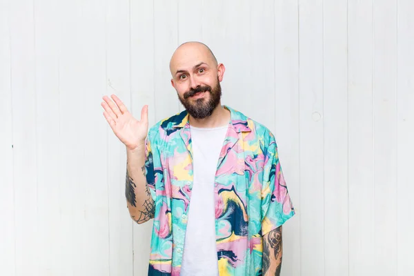 bald man smiling happily and cheerfully, waving hand, welcoming and greeting you, or saying goodbye