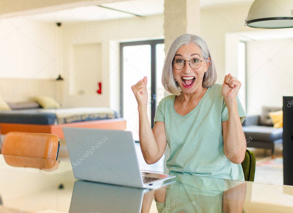 middle age woman feeling happy, surprised and proud, shouting and celebrating success with a big smile