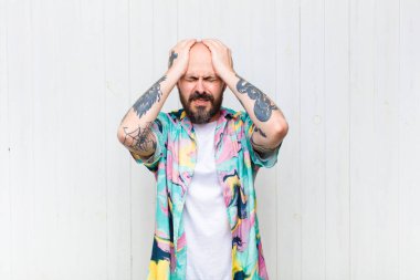 Kel bir adam stresli ve endişeli, depresif ve hayal kırıklığına uğramış hissediyor, iki elini de başa kaldırıyor.