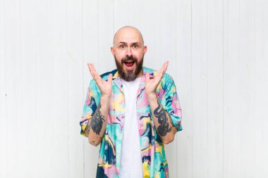 Kel adam mutlu ve heyecanlı görünüyor. Beklenmedik bir sürprizle şoke olmuş. İki eli yüzü açık.