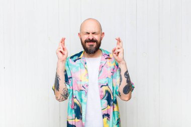 Kel adam gülümsüyor ve endişeyle iki parmağını çapraz yapıyor. Endişeli ve iyi şanslar diliyor.