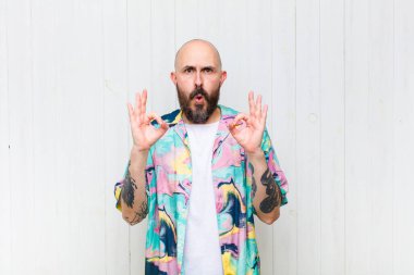 Kel adam şok olmuş, şaşırmış ve şaşırmış hissediyor. Onaylıyor. İki eliyle de onay işareti yapıyor.