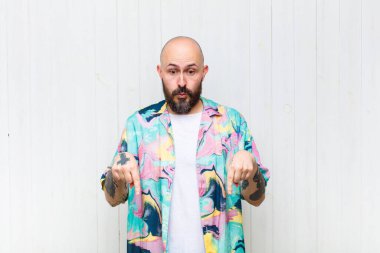 Kel ve ağzı açık bir adam iki eliyle aşağıya doğru bakıyor, şaşkın, şaşkın ve şaşırmış görünüyor.