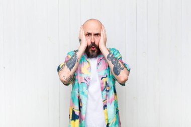 Kel adam mutsuz, korkmuş ya da endişeli görünüyor, ağzı sonuna kadar açık ve iki kulağını da elleriyle kapatıyor.