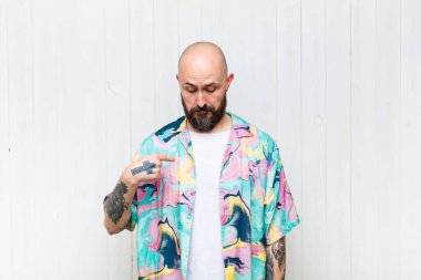 Kel adam neşeyle gülümsüyor, yere bakıyor ve göğsünü işaret ediyor.