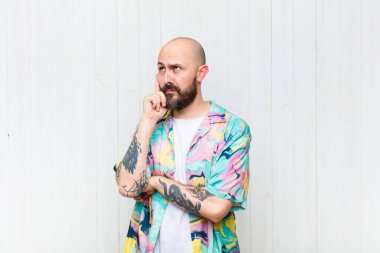 Yoğunlaşmış bakışları olan kel bir adam şüpheli bir ifadeyle yukarı ve yana bakıyor.