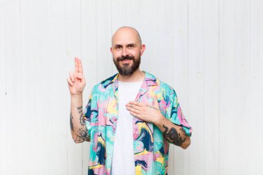 Kel adam mutlu, kendinden emin ve güvenilir görünüyor, gülümsüyor ve zafer işareti gösteriyor, olumlu bir tavırla.