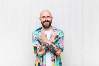 Kel adam neşeyle gülümsüyor ve kutluyor, yumruklarını sıkıp kollarını kavuşturuyor, mutlu ve pozitif hissediyor.