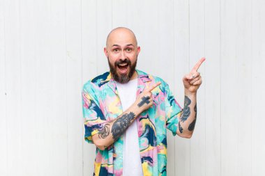 Kel adam mutlu ve şaşırmış hissediyor, şok olmuş bir ifadeyle gülümsüyor ve yan tarafı işaret ediyor.