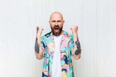 Kel adam öfkeli bir ifadeyle ya da yumruklarıyla başarıyı kutlarken agresif bir şekilde bağırıyor.